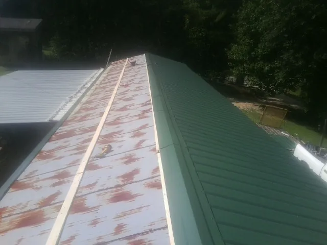Old rusted panels beside newly installed green metal roofing — Wind Damage Roof Repair by Roofing Brothers in Jewell